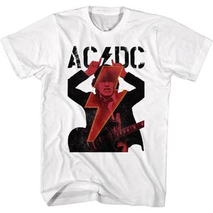 May include: White t-shirt featuring a graphic of a musician with a red lightning bolt and the band name AC/DC in black block letters. The musician is playing a guitar. The shirt is a short-sleeved crew neck.
