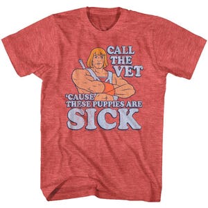 May include: Red heather t-shirt featuring a cartoon illustration of a muscular character with a sword. The text on the shirt reads "CALL THE VET" above "'CAUSE THESE PUPPIES ARE SICK".