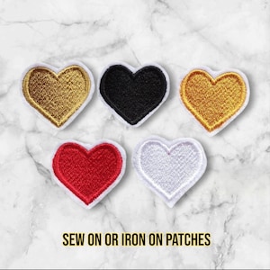 May include: Five iron-on or sew-on heart-shaped patches in different colours: gold, black, gold, red, and white.