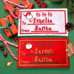 May include: Two Christmas gift tags, one white and one red, with embroidered text and Santa Claus designs. The white tag says "Ho Ho Ho Amelia From Santa." The red tag says "Ho Ho Ho Aaron From Santa."