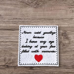 May include: White square embroidered with black text that reads "Never said goodbye because I have my eye looking at your face filled with memories." A red heart is embroidered below the text. The square has a black scalloped border.