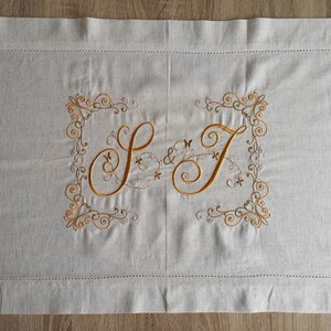 May include: A white linen pillowcase with gold embroidery of the letters "S & J" in a decorative script font. The letters are surrounded by a floral design.