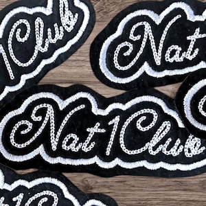 May include: Black embroidered patches with white stitching. The patches are in a cloud shape and feature the words "Club" and "Nat 1 Club". The patches are on a wooden surface.