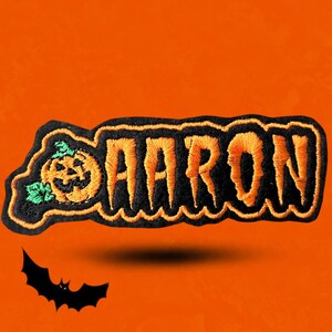 May include: Embroidered patch with the name "AARON" in orange, outlined in black, with a jack-o'-lantern on the left side. The patch has a black border and is set against an orange background, with a black bat silhouette.
