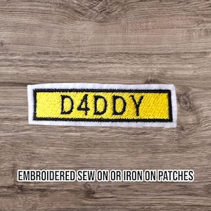 May include: Embroidered patch with the word "D4DDY" in black letters on a yellow background, framed by a black border and a white edge. The text "EMBROIDERED SEW ON OR IRON ON PATCHES" is below.