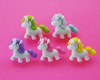 May include: Five white unicorn figurines with different colored manes and tails. The unicorns are arranged in a semi-circle on a pink background.