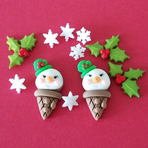 May include: Two white snowman ice cream cone ornaments with green holly hats and brown cones. The ornaments are surrounded by white snowflake and green holly leaf ornaments on a red background.