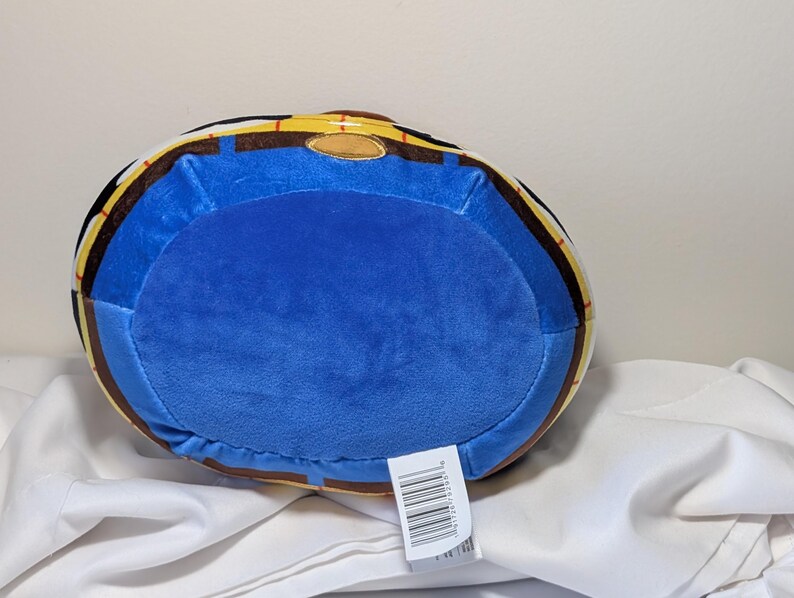 May include: A plush toy in the shape of a barrel, featuring a blue center and a yellow and brown rim. The toy has a soft, velvety texture and a tag with a barcode.
