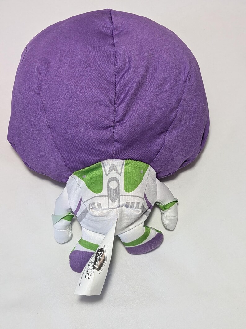 May include: A plush toy of Buzz Lightyear from Toy Story, featuring a large purple head and a white and green spacesuit. The toy has a tag with the Disney logo.