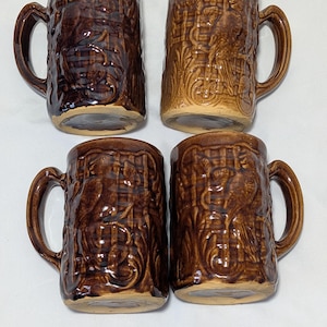 Pode incluir: Quatro canecas de cerâmica marrom com alças. Cada caneca apresenta um design em relevo detalhado de um pássaro e folhagem. As canecas têm um acabamento brilhante e uma cor marrom escuro.