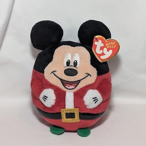 May include: A round Mickey Mouse Beanie Ballz plush toy. Mickey is wearing a red Santa suit with a black belt and gold buckle. The plush has black ears, a white face, and a red heart-shaped tag.