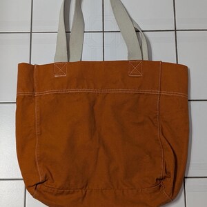 May include: A large, brown canvas tote bag with white straps. The bag has a simple design and is perfect for carrying everyday essentials.