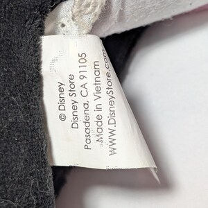May include: Close-up of a white tag with black text from the Disney Store. The tag reads "&copy; Disney Disney Store Pasadena, CA 91105 Made in Vietnam www.DisneyStore.com" and is attached to a black plush toy.