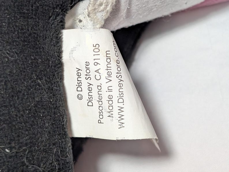 May include: Close-up of a white tag with black text from the Disney Store. The tag reads "&copy; Disney Disney Store Pasadena, CA 91105 Made in Vietnam www.DisneyStore.com" and is attached to a black plush toy.