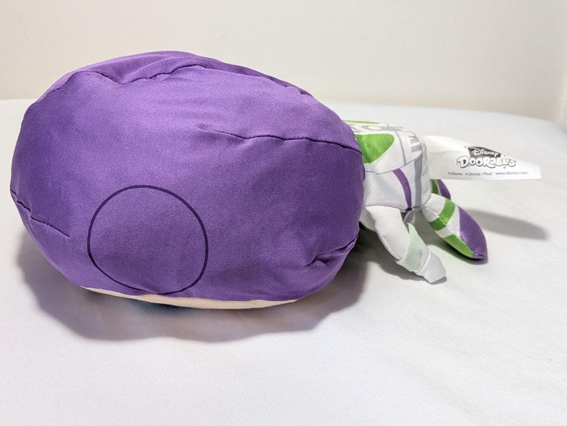 May include: A plush toy of Buzz Lightyear from Disney's Toy Story. The toy features a large purple head with a circular design, and white and green arms. A Disney Doorables tag is attached.