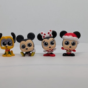 May include: Four small cartoon character figurines. Pluto is yellow with a green collar. Mickey Mouse is black and red. Minnie Mouse has a red and white polka dot bow. The last figure is Mickey Mouse in a Santa hat.