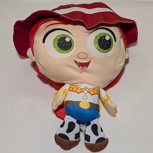 May include: A plush doll of a character with red hair and a matching hat. The doll has large green eyes, a tan face, and a white shirt with a yellow collar. The doll's blue trousers have black and white spots. The doll is a character from a popular animated film.
