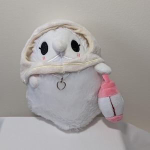 May include: A white plush toy with a hooded cloak and a silver heart pendant. The toy has black eyes, pink cheeks, and a small pink and white lantern. The plush is soft and fluffy.