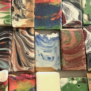 May include: Assortment of handmade soap bars with various colors and patterns, including blue, green, red, brown, and white.
