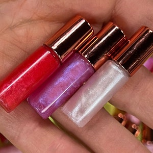 May include: Four lip glosses in clear tubes with rose gold caps. The glosses are red, pink with iridescent shimmer, and two shades of white with iridescent shimmer.
