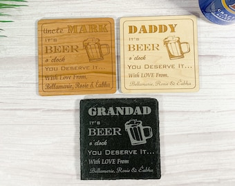 May include: Three wooden coasters with a beer mug design and the text "It's Beer o'clock" with personalized names "Uncle Mark", "Daddy", and "Grandad". Each coaster has the text "You Deserve It... With Love From, Bellamarie, Rosie & Éabha".