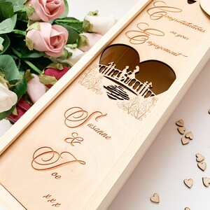 May include: Wooden box with a heart-shaped cutout featuring a couple on a bridge. The box is engraved with the text "Congratulations on your engagement" and the names "Susanne & Dave".