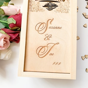 May include: A wooden box with a personalised inscription that reads "Susanne & Joe xxx". The box is decorated with a floral design and a heart motif.