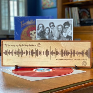 May include: A wooden plaque with a sound wave graphic and the text "My time coming any day don't worry about me" and "ESTIMATED PROPHET - GRATEFUL DEAD".