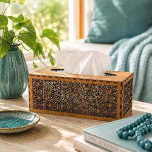 May include: A rectangular wooden tissue box cover featuring a laser-cut geometric star pattern on the sides and top. The box is constructed with visible interlocking joints at the corners and holds a stack of white facial tissues.