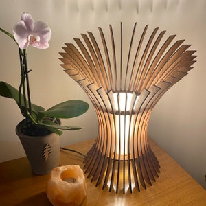 May include: A wooden table lamp with a unique, openwork design. The lamp has a flared base and a top that resembles a blooming flower. A potted orchid and a Himalayan salt candle holder are also visible.