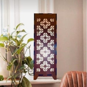 May include: A wooden table lamp with a decorative floral cutout design. The lamp is lit and casts a warm glow.