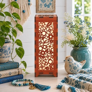 Op de afbeelding: Een rechthoekige houten lamp met een bloemenpatroon. De lamp heeft een warme gloed van het licht binnenin. Het frame is een rijke bruine kleur en de bloemenuitsparingen zijn ingewikkeld. Een decoratief woonaccessoire.