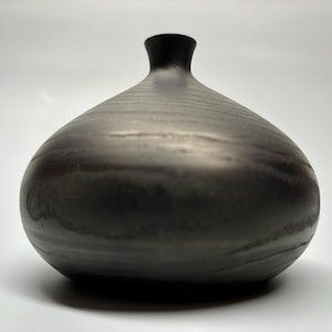 May include: A black ceramic vase with a rounded, bulbous shape and a narrow neck. The vase has a smooth, glossy finish.