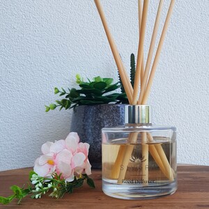May include: A clear glass bottle with a silver lid and brown liquid inside. The bottle has a label that says "Siyara Reed Diffuser".  The bottle is surrounded by natural wooden sticks.