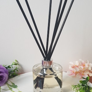 May include: A clear glass bottle with a silver lid and black reeds. The bottle is filled with a light yellow liquid and has a label that says "Reed Diffuser".