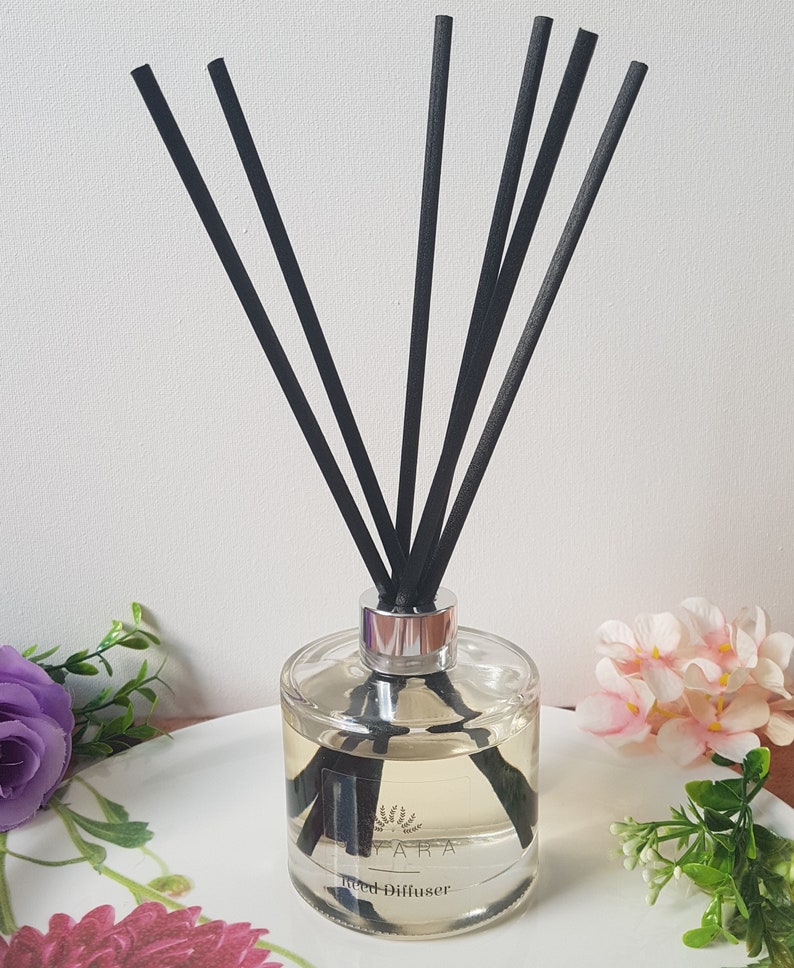 May include: A clear glass bottle with a silver lid and black reeds. The bottle is filled with a light yellow liquid and has a label that says "Reed Diffuser".