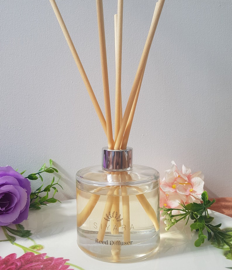 May include: A clear glass bottle with a silver lid and wooden sticks, filled with a light yellow liquid. The bottle has a label that reads "Siyara Reed Diffuser".