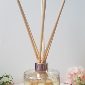 May include: A clear glass bottle with a silver lid and wooden sticks, filled with a light yellow liquid. The bottle has a label that reads "Siyara Reed Diffuser".