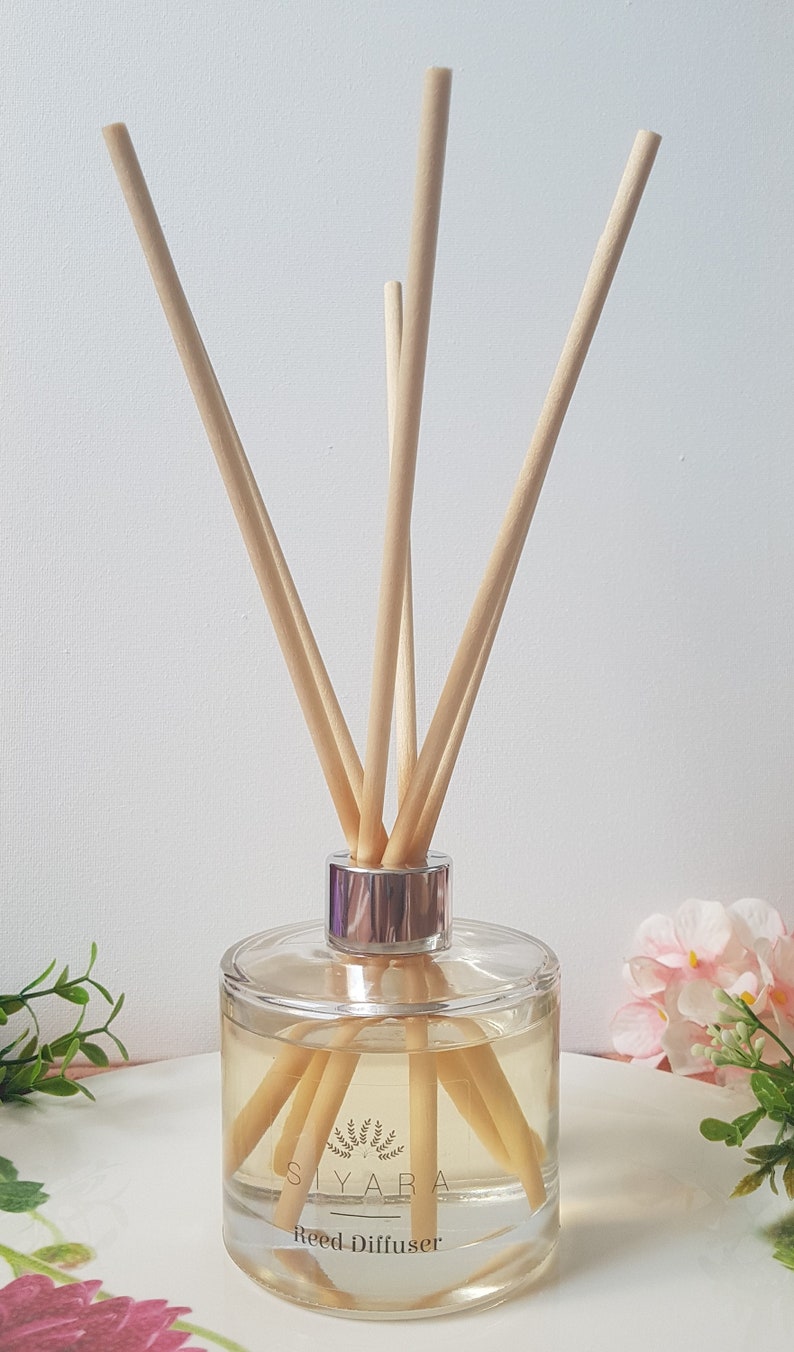 May include: A clear glass bottle with a silver lid and wooden sticks, filled with a light yellow liquid. The bottle has a label that reads "Siyara Reed Diffuser".