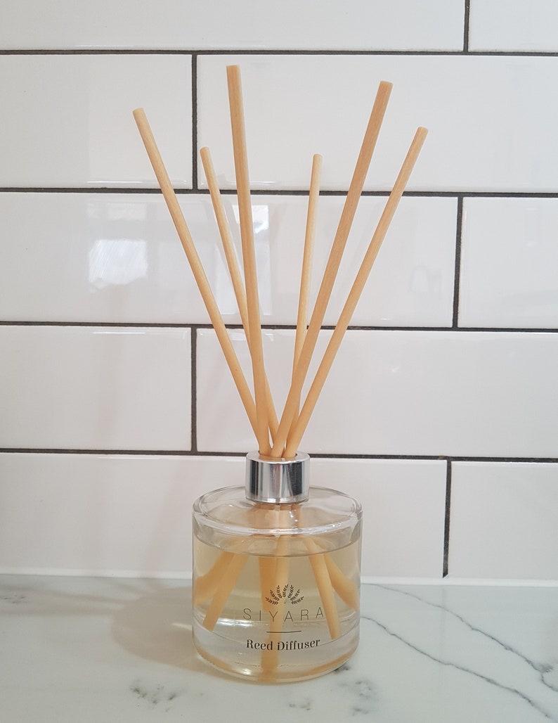 May include: A clear glass bottle with a silver lid and natural reed diffuser sticks. The bottle contains a light yellow liquid and has a label that reads "Siyara Reed Diffuser".