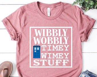 Puede incluir: Una camiseta rosa con un gráfico blanco que dice "Wibbly Wobbly Timey Wimey Stuff" con un TARDIS azul en el medio del texto.