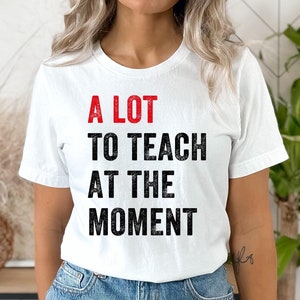 May include: White t-shirt with the text "A LOT TO TEACH AT THE MOMENT" in black and red lettering.