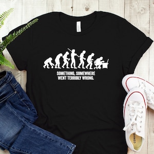 May include: Black t-shirt with a white graphic of the evolution of man ending with a person sitting at a computer. The text below the graphic reads "Something, somewhere went terribly wrong."