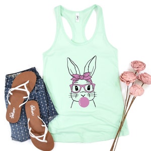May include: A mint green tank top with a graphic of a cartoon bunny wearing pink glasses and a pink headband, blowing a pink bubble.