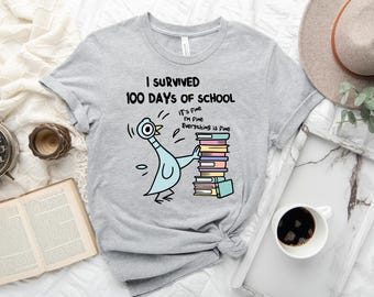 May include: Light gray t-shirt with the text "I Survived 100 Days of School" and a cartoon pigeon character. The pigeon is holding a stack of books. The shirt also has the text "It's Fine, I'm Fine, Everything is Fine."