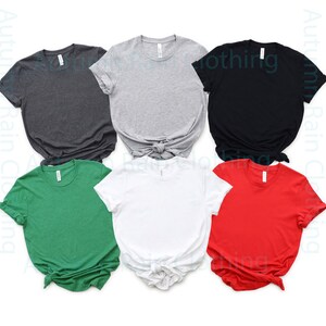 May include: Six blank t-shirts in different colours: dark grey, light grey, black, green, white, and red. The shirts are folded and laid out on a white background.