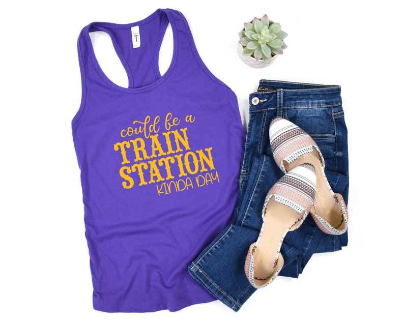 May include: Purple tank top with a yellow graphic that says "could be a train station kinda day".