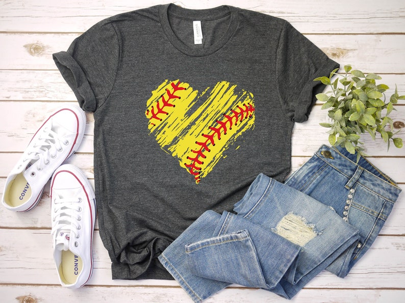 May include: A dark gray t-shirt with a yellow and red softball design in the shape of a heart. The softball has red stitching and is on a white background.