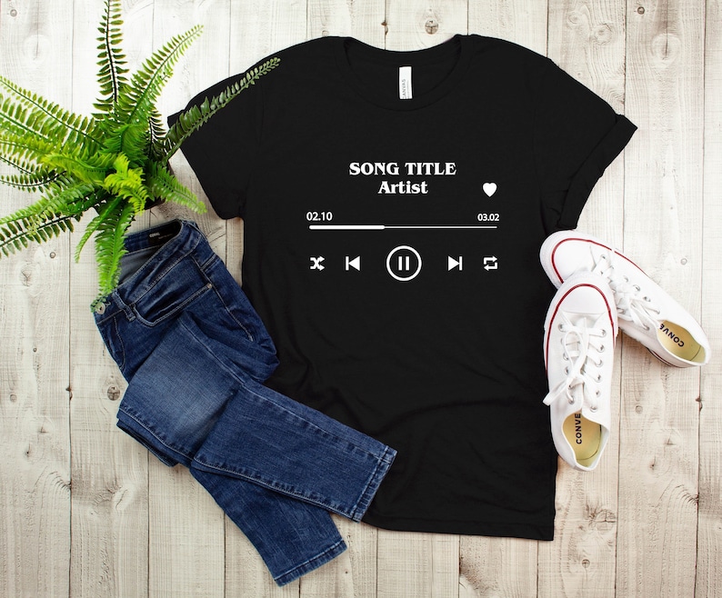 May include: Black t-shirt with a white graphic of a music player with the text "SONG TITLE Artist" and a heart icon. The player shows the time 02:10 and 03:02, and has play, pause, rewind, and fast forward buttons.