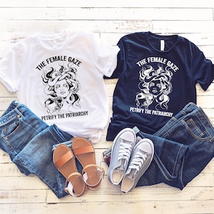 May include: Two t-shirts with a black and white graphic of a Medusa-like figure with snakes for hair. The text on the shirts reads "The Female Gaze" and "Petrify the Patriarchy". One shirt is white and the other is black.